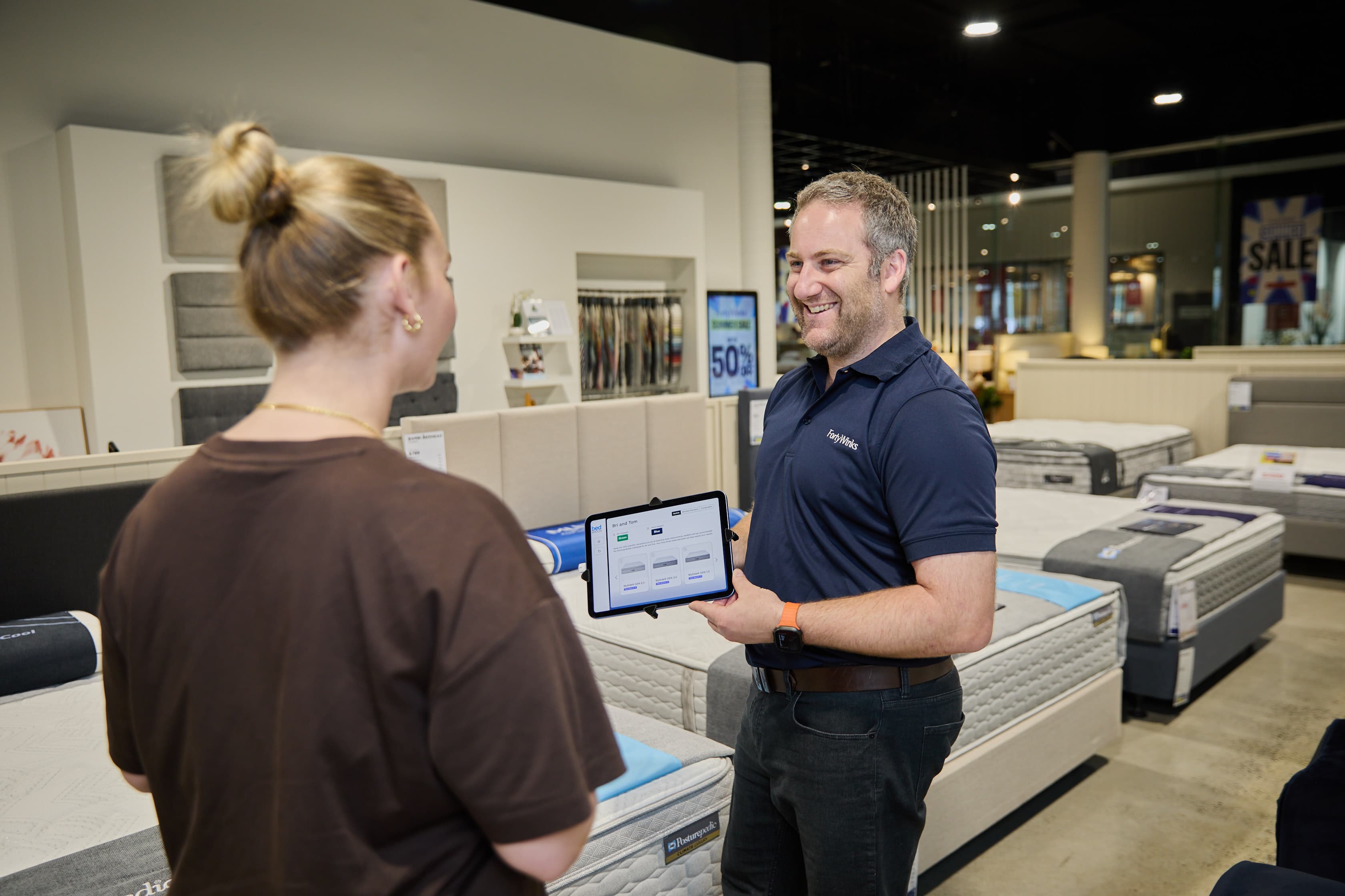 Forty Winks team member using a tablet to help a customer choose a mattress.