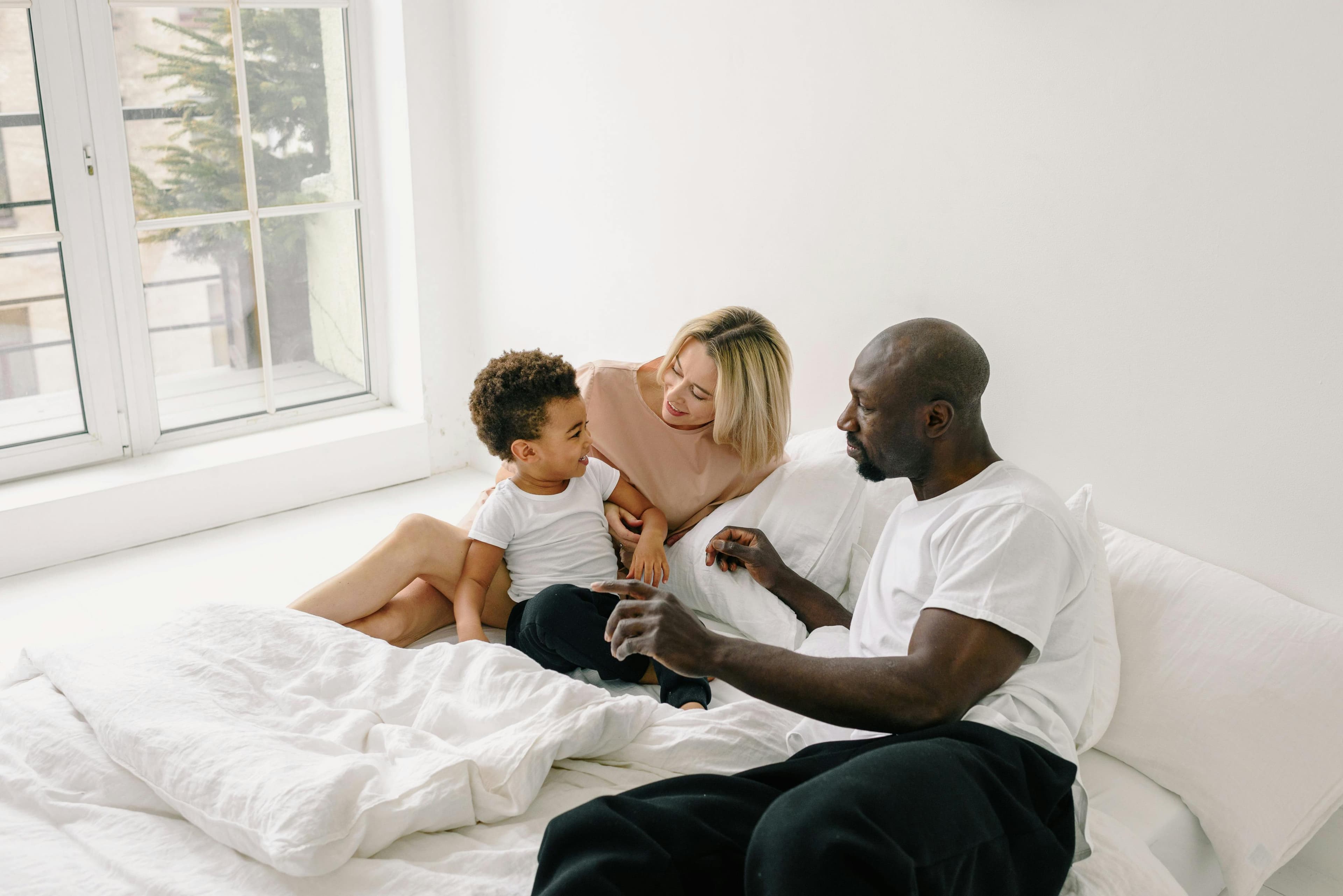 Parents and their young son laughing together on a bed.
