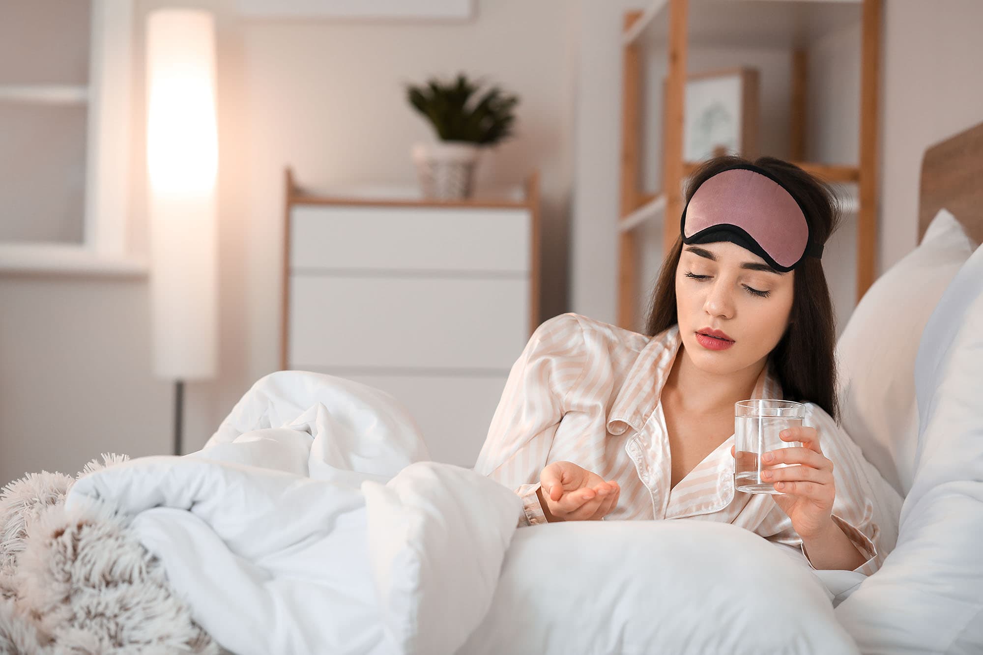 Woman in bed taking a supplement with a glass of water.
