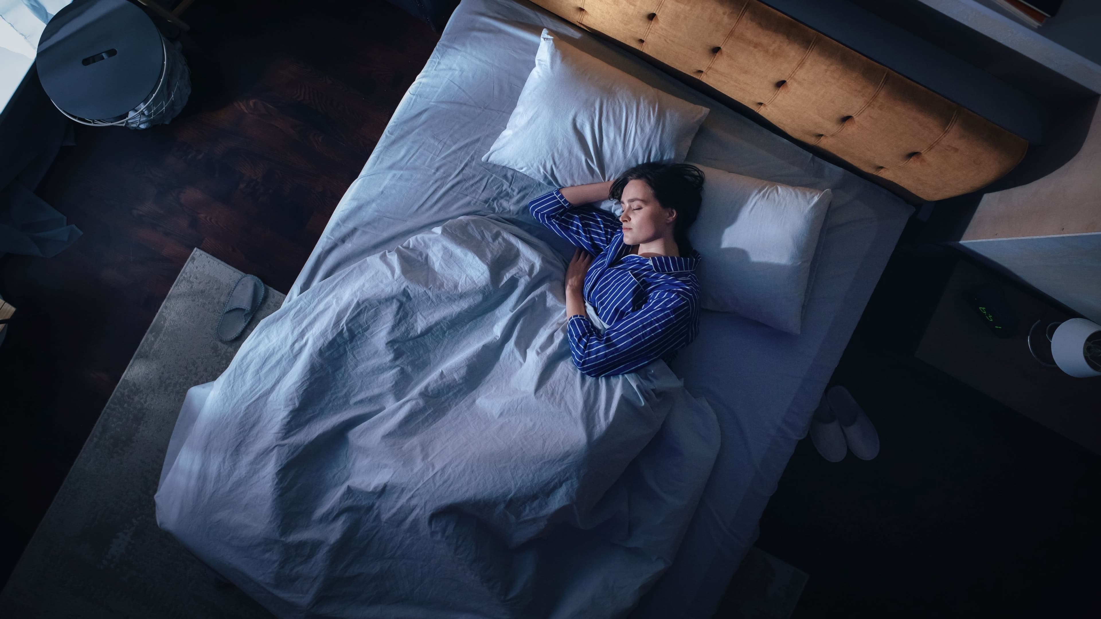 Woman fast asleep in a dark bedroom, seen from above.