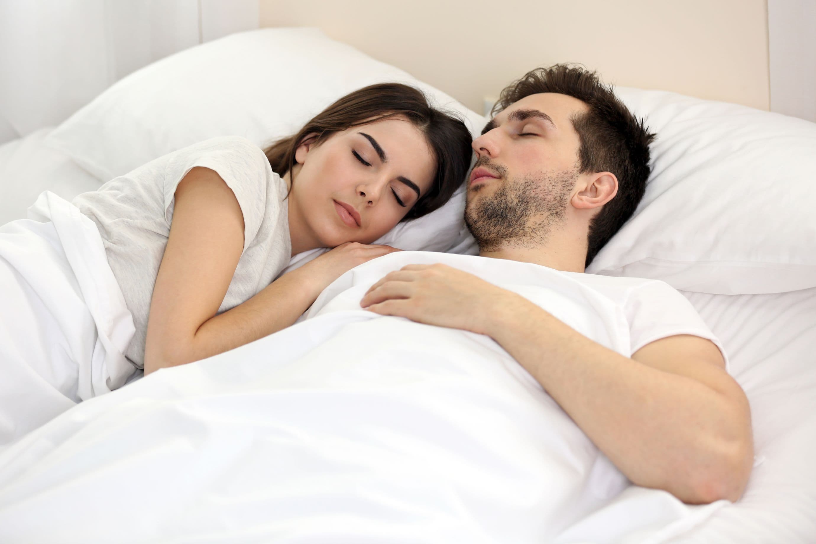 Couple sleeping side by side under white bedding