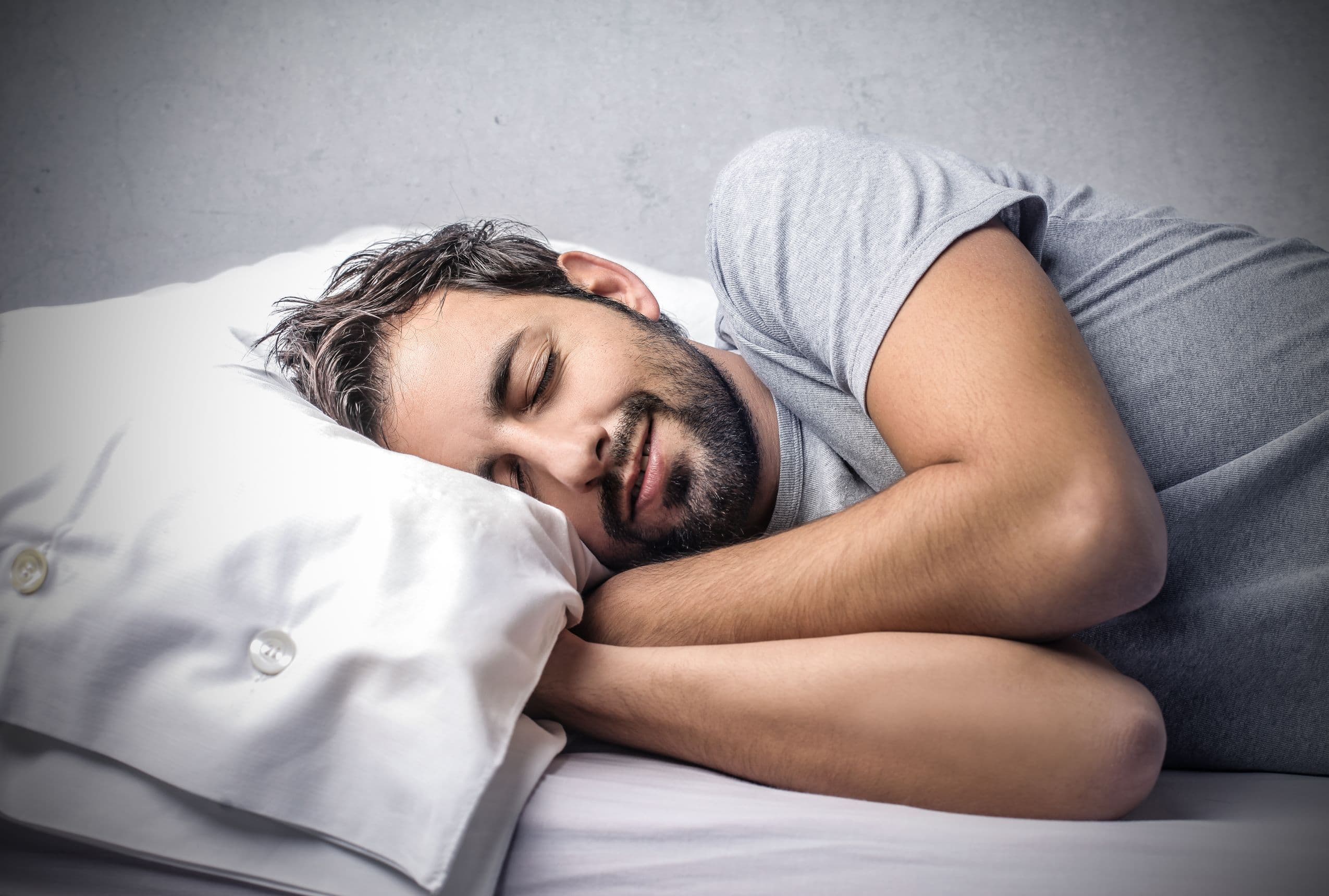 Smiling bearded man sleeping on his side on a white pillow