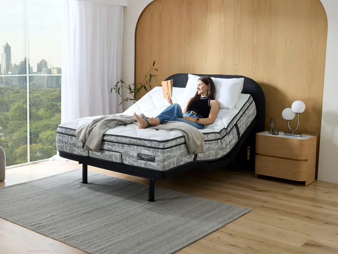 Woman reading on an adjustable bed in a bright city apartment.