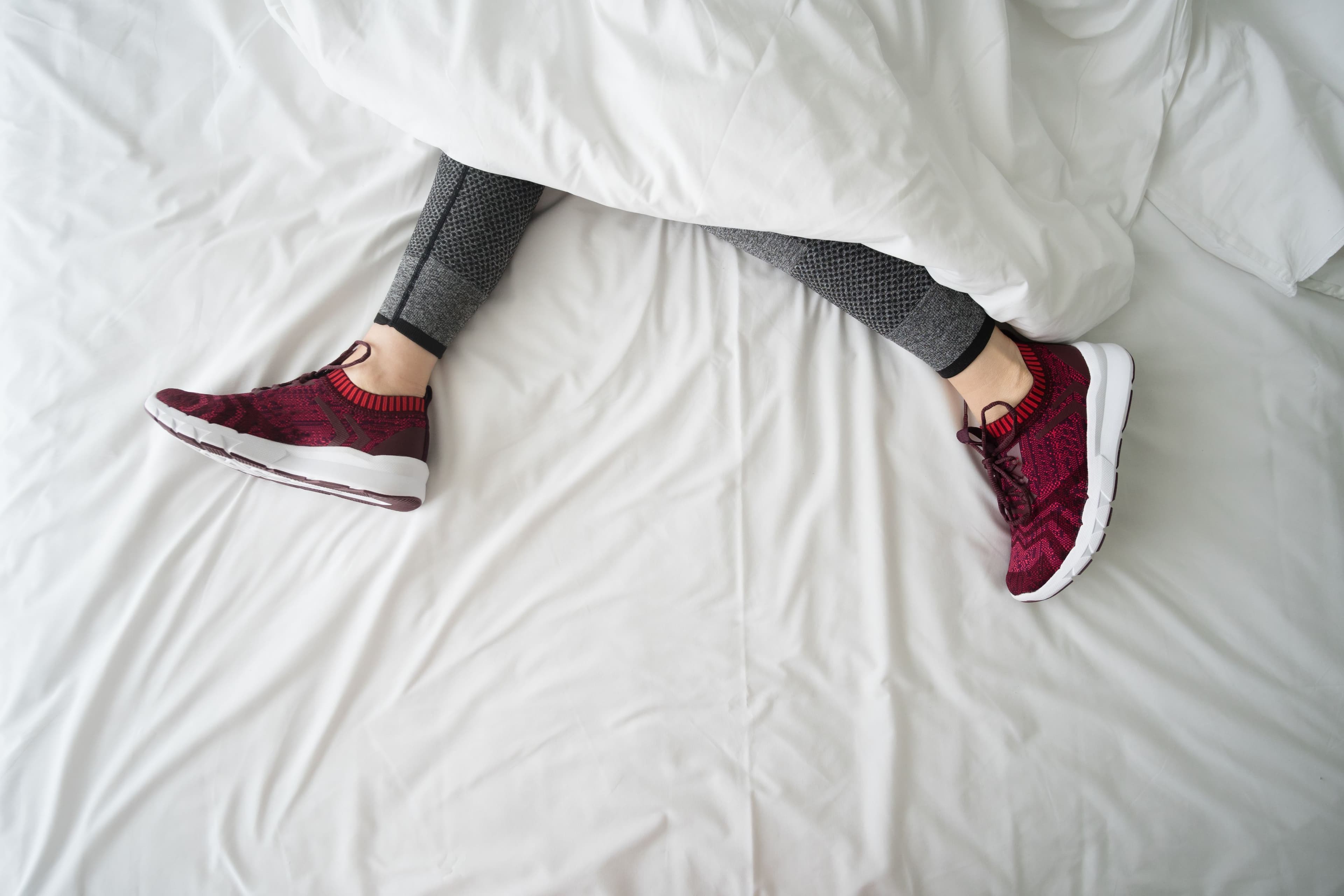 Legs in running shoes stretched out on a bed under the covers.