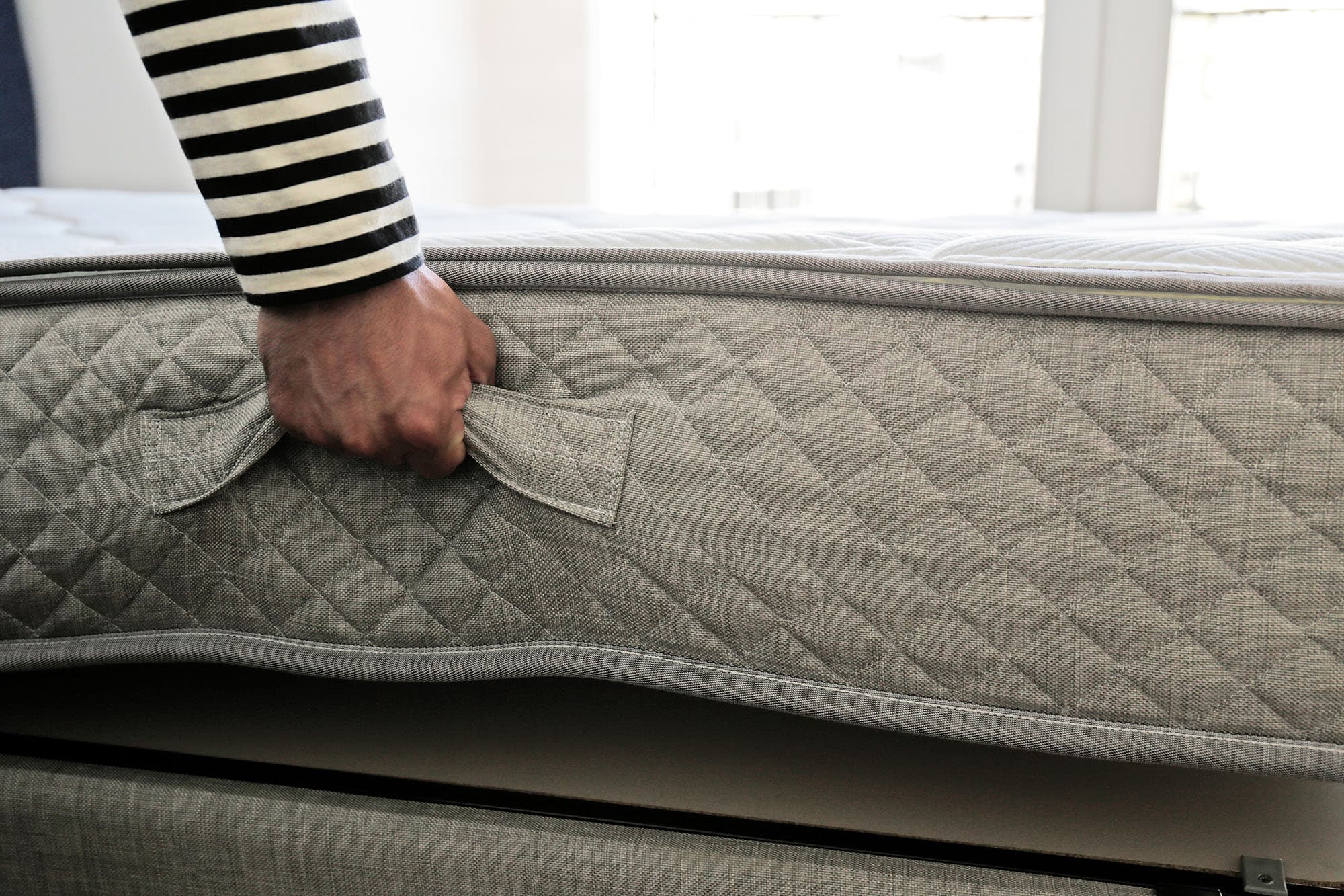 Hand gripping a mattress handle to rotate it.