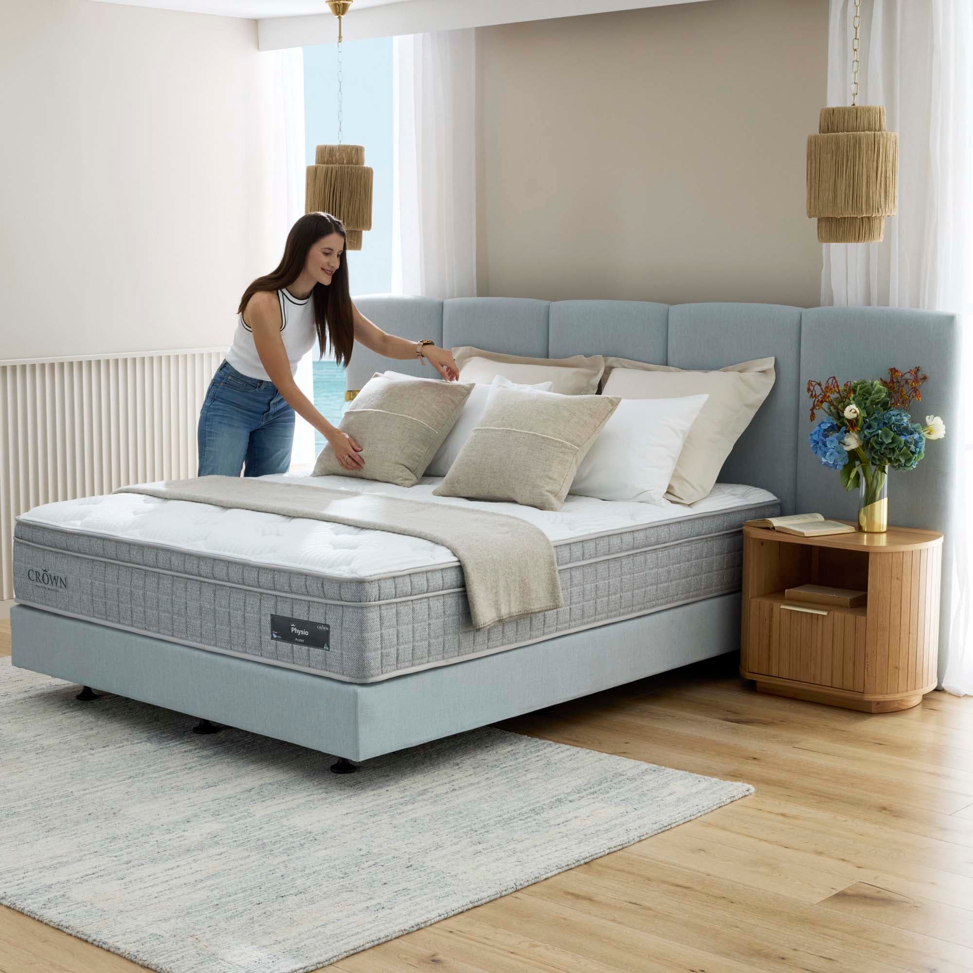 Woman arranging pillows on a supportive mattress in a bright bedroom.