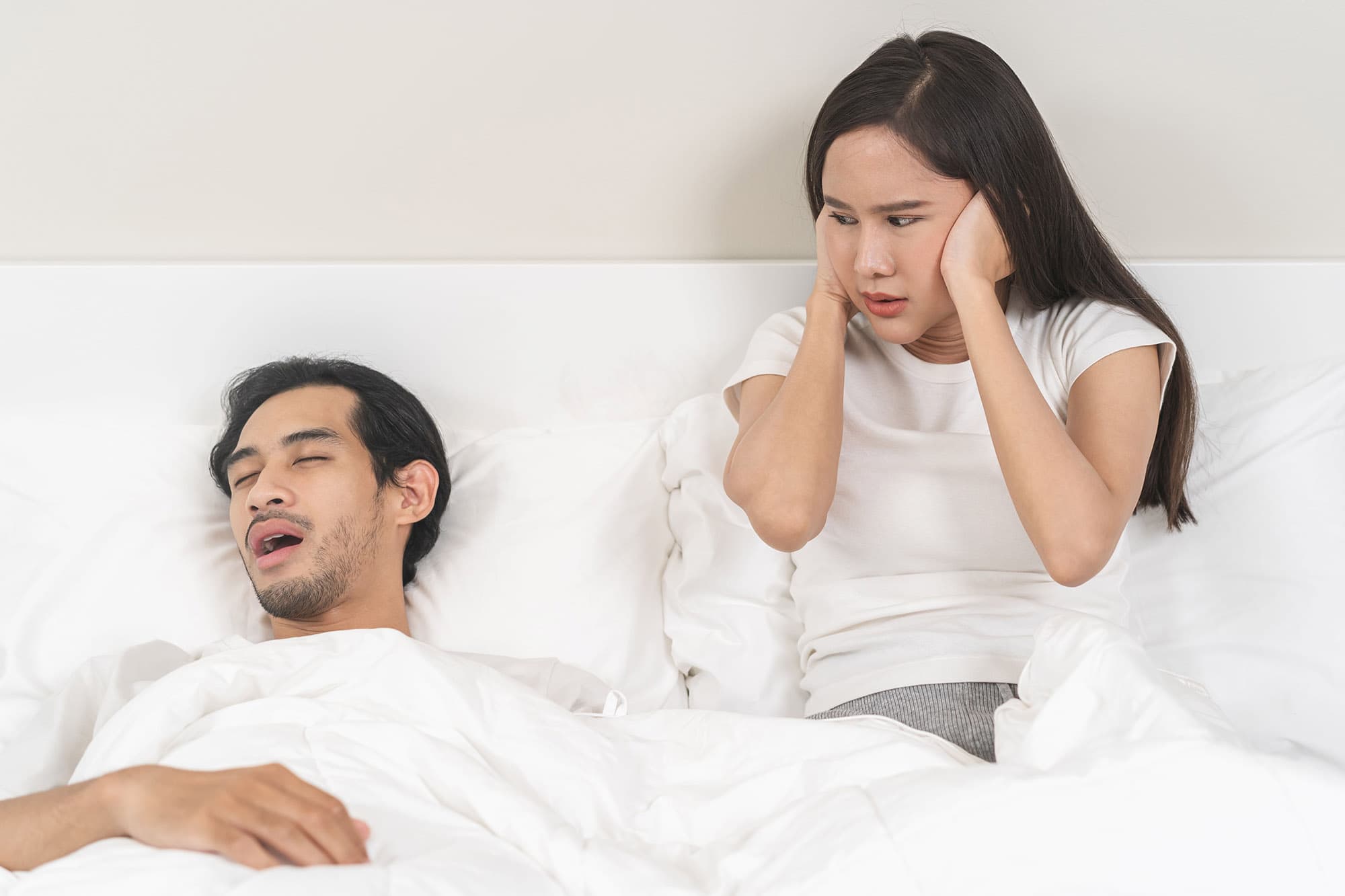 Man snoring with his mouth open while his partner covers her ears.