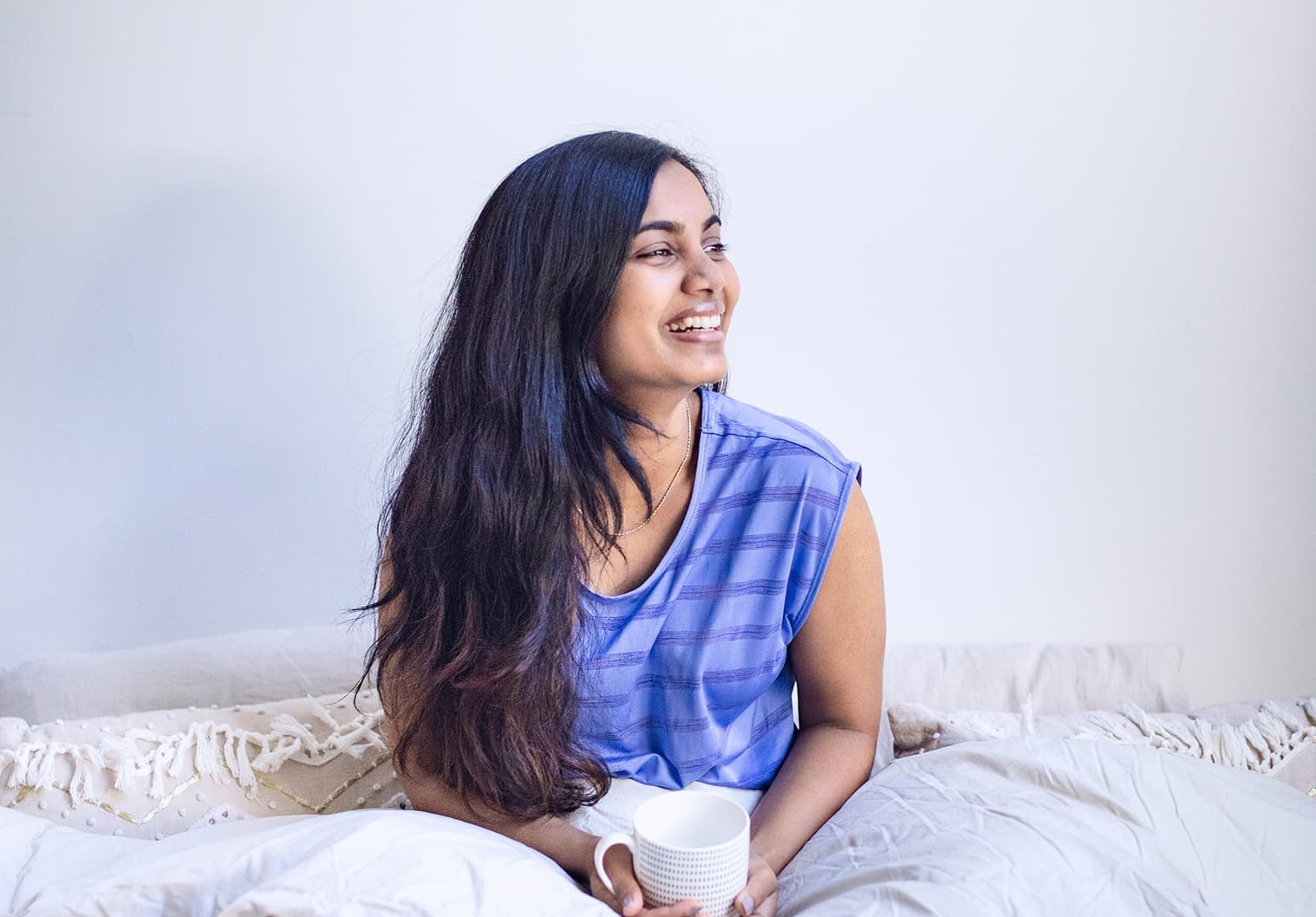Woman sitting up in bed with a cup of tea, smiling.
