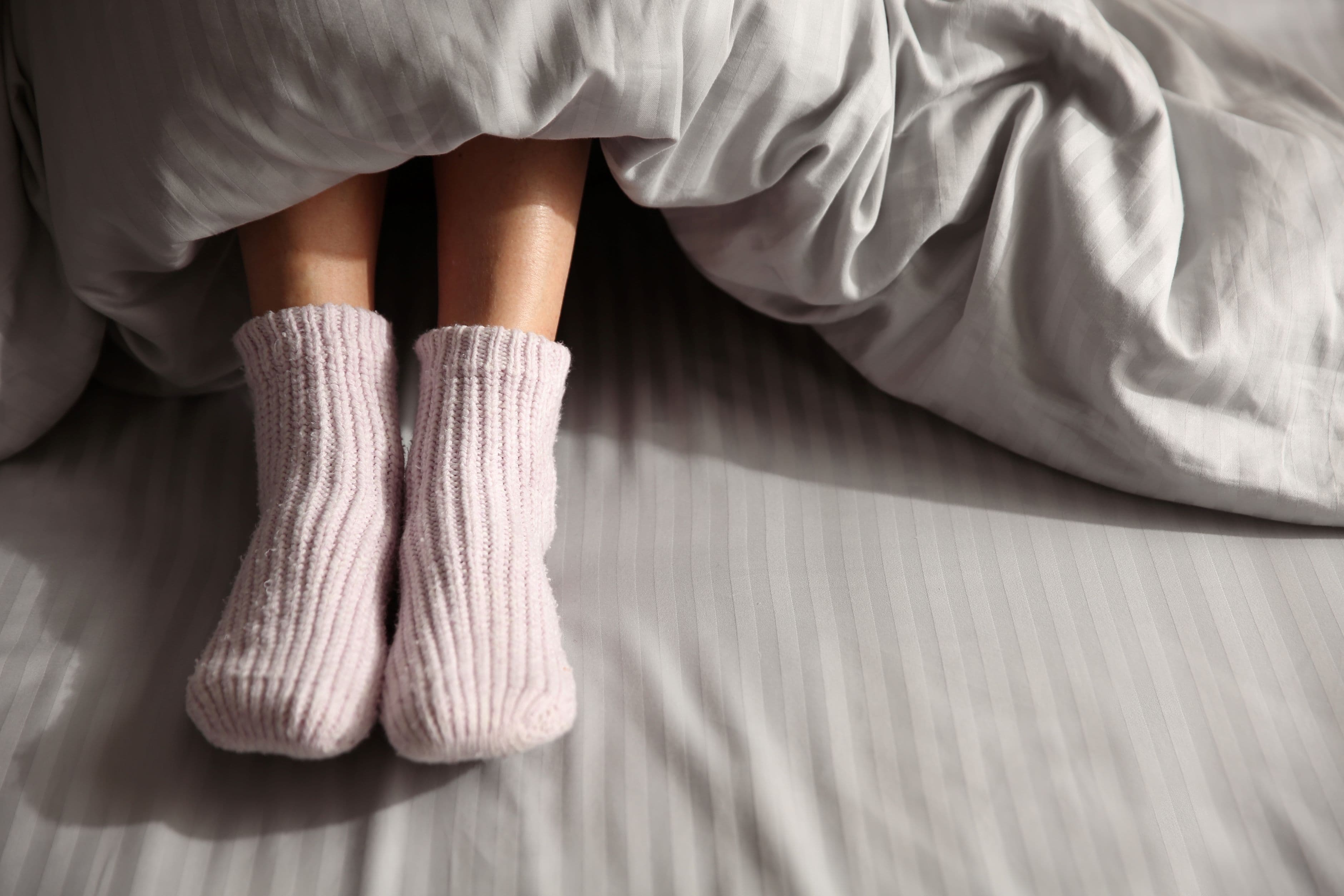Feet in pink knitted socks poking out from under a grey doona