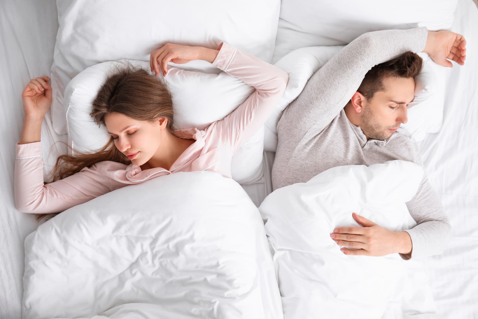 Couple sleeping side by side, short on space in a smaller bed.