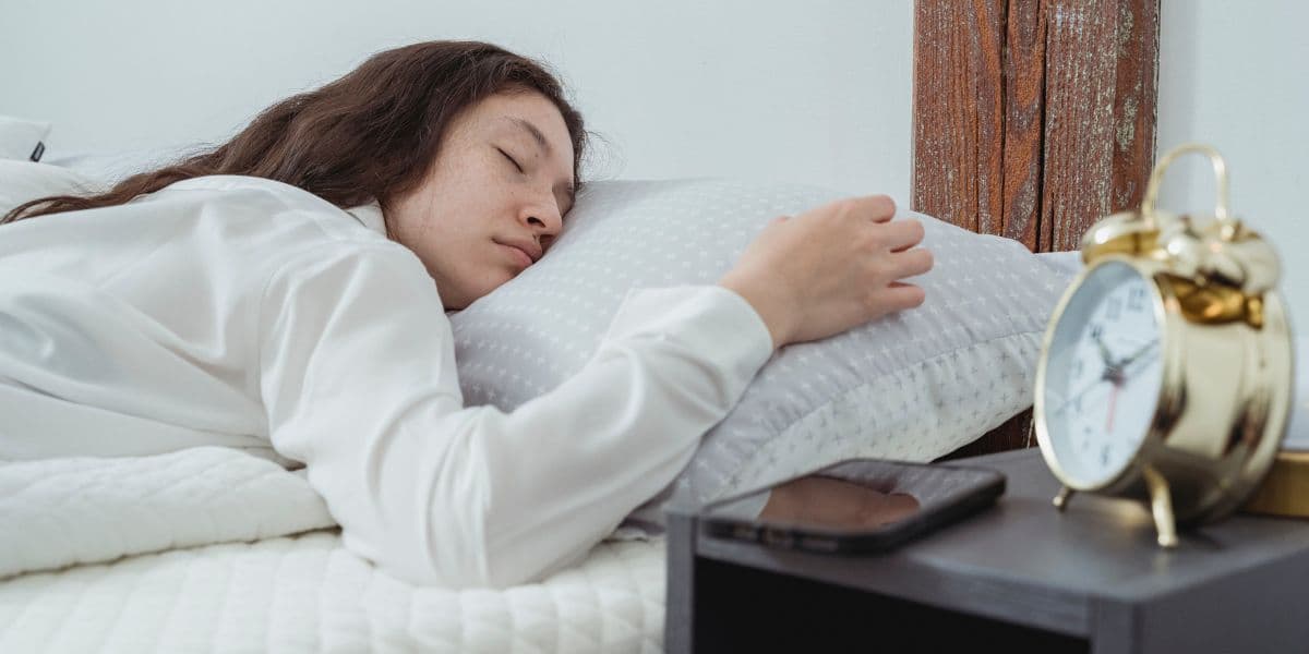 Woman asleep with her phone put away on the bedside table.
