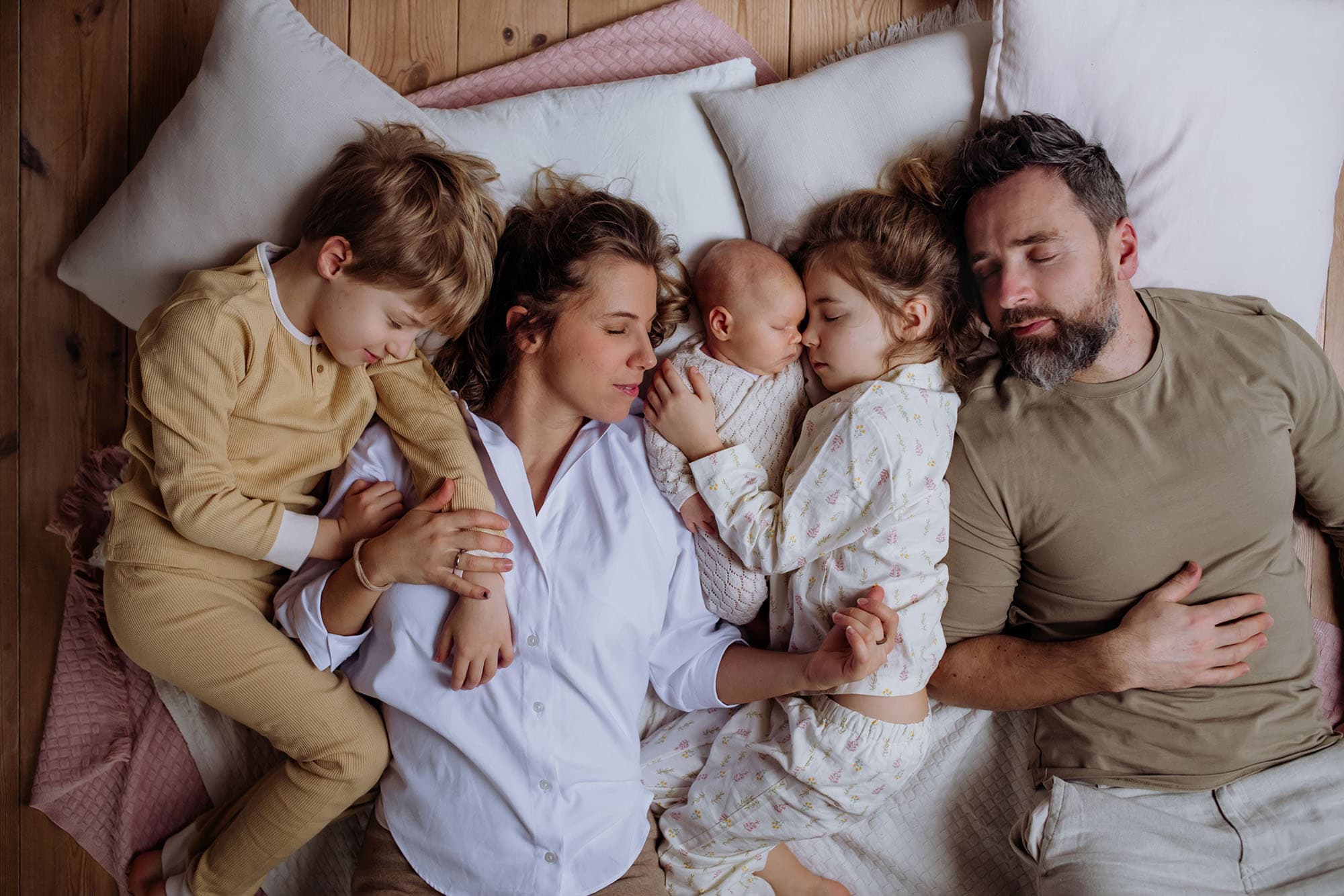 Parents and three young children sleeping together on pillows on the floor